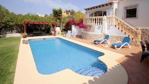 Une piscine avec des chaises longues, un patio couvert et un escalier menant à une maison équipée d’une antenne parabolique.