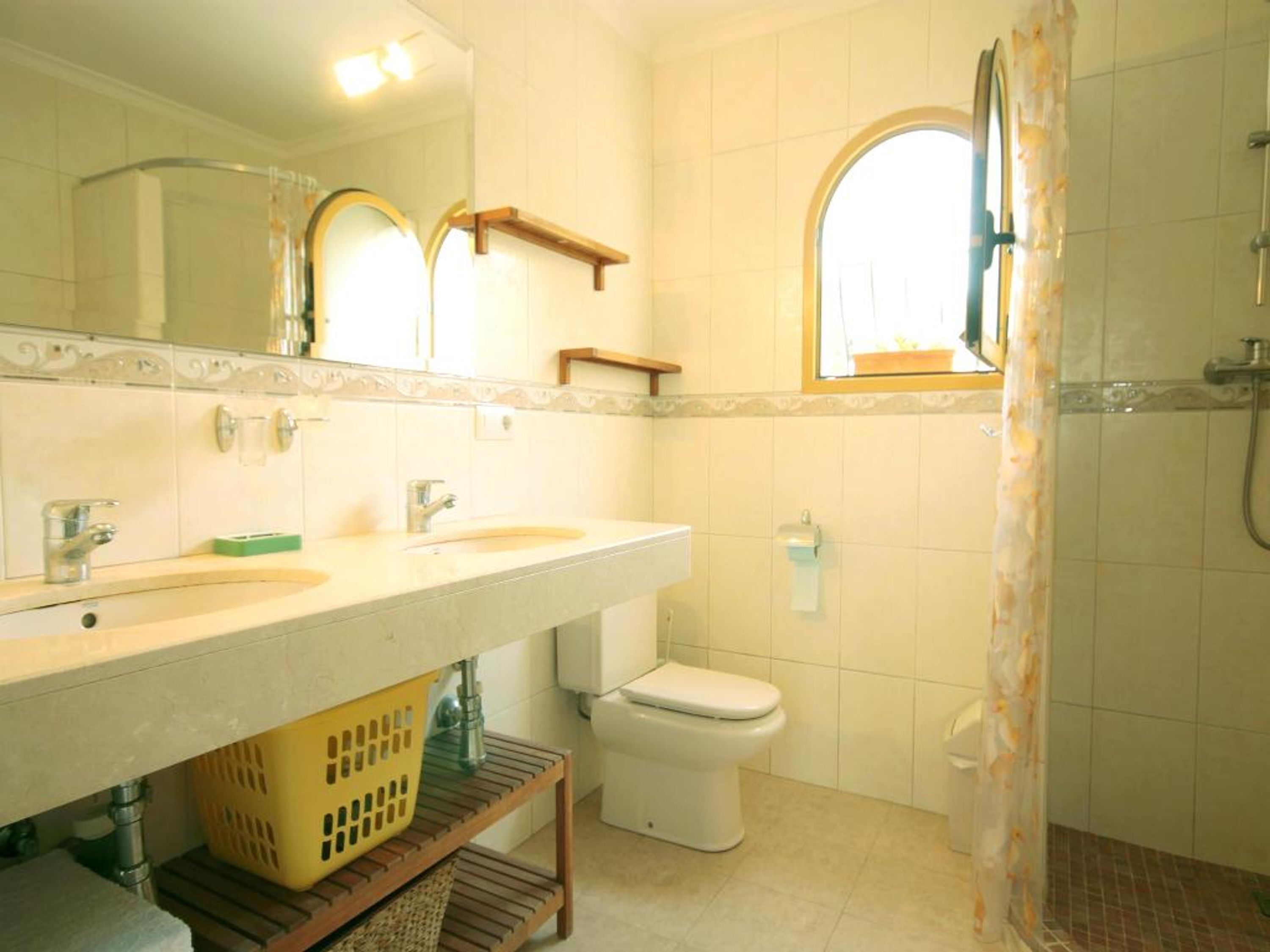 A bathroom with a sink, mirror, toilet, shower, and a window.