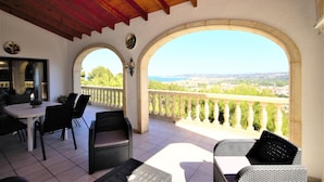 A covered patio with a table and chairs, a view of the city, and a balcony with a railing. - Villa- Impala in Javea (Javea)