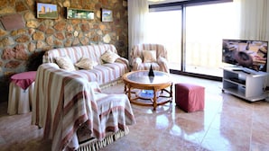 A living room with a stone wall, a sofa set, a coffee table, and a television. - Villa- Impala in Javea (Javea)