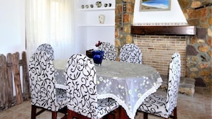A dining area with a table set for four, surrounded by patterned chairs, a chandelier, and a stone fireplace. - Villa- Impala in Javea (Javea)