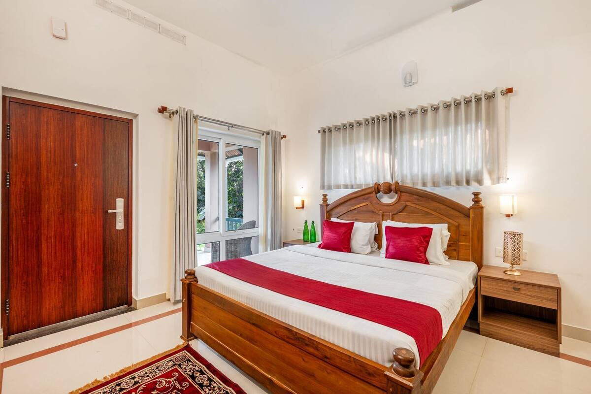 A bedroom with a wooden bed, a nightstand, a window with curtains, and a door.