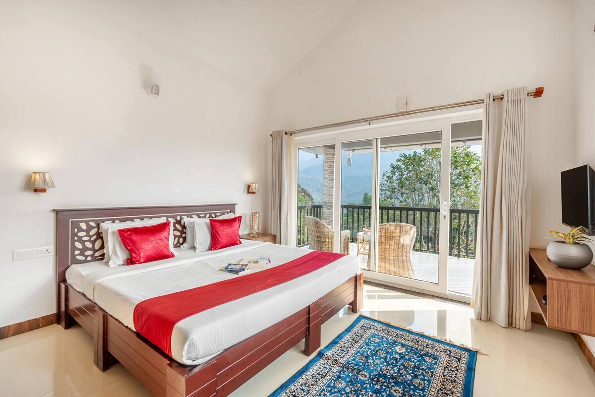 A bedroom with a bed, a view of the outdoors, a TV, and a window with curtains.