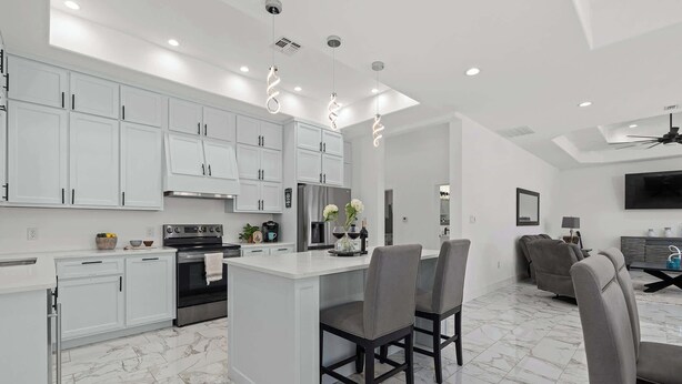 A modern kitchen with white cabinets, a central island with chairs, and a dining area with a sofa and TV. - Charming Family Getaway Near Medina River! (Bandera)