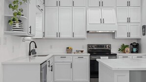 A modern kitchen with white cabinetry, a stainless steel range hood, and a black stove. - Charming Family Getaway Near Medina River! (Bandera)