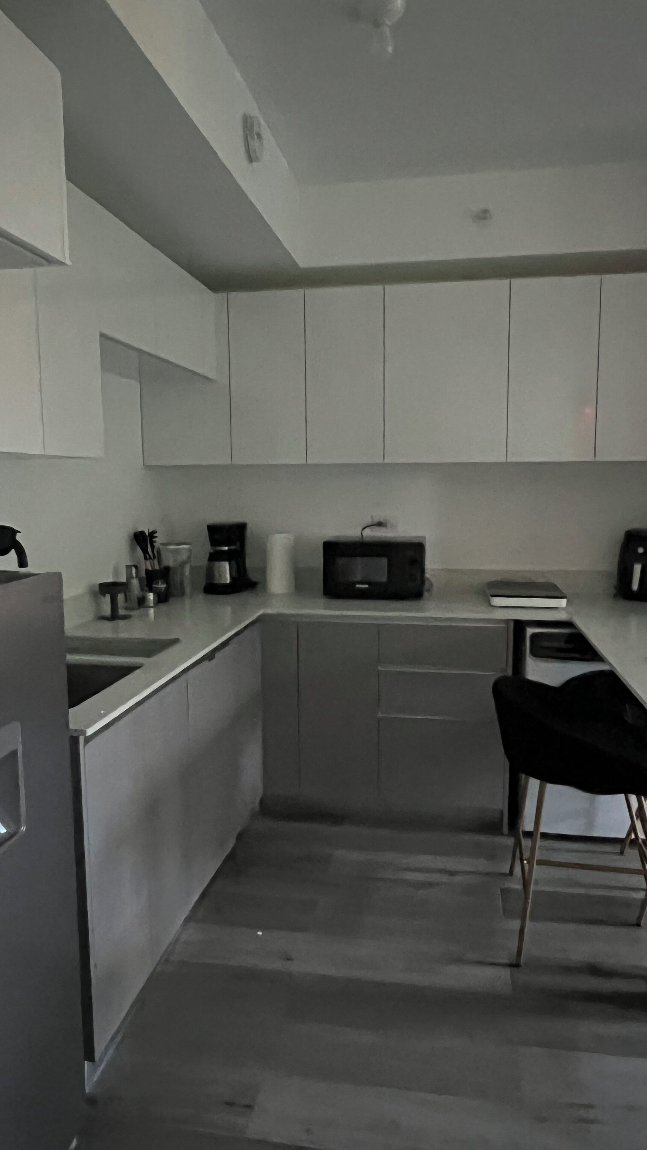 A modern kitchen with white cabinets, a microwave, a coffee maker, and a black chair.