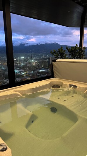 Un jacuzzi con vista a la ciudad, amplios ventanales y una planta.