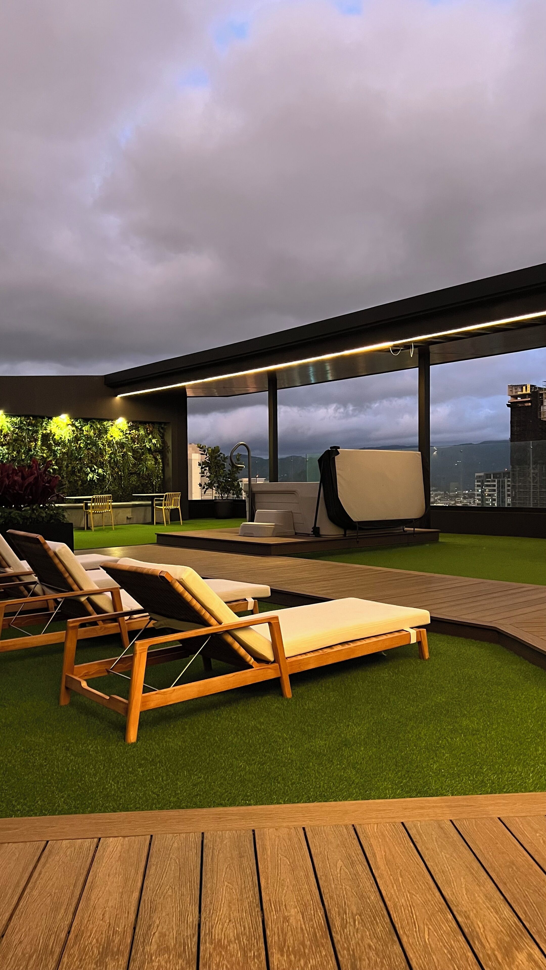 A rooftop terrace with wooden lounge chairs, a hot tub, and a view of the cityscape.