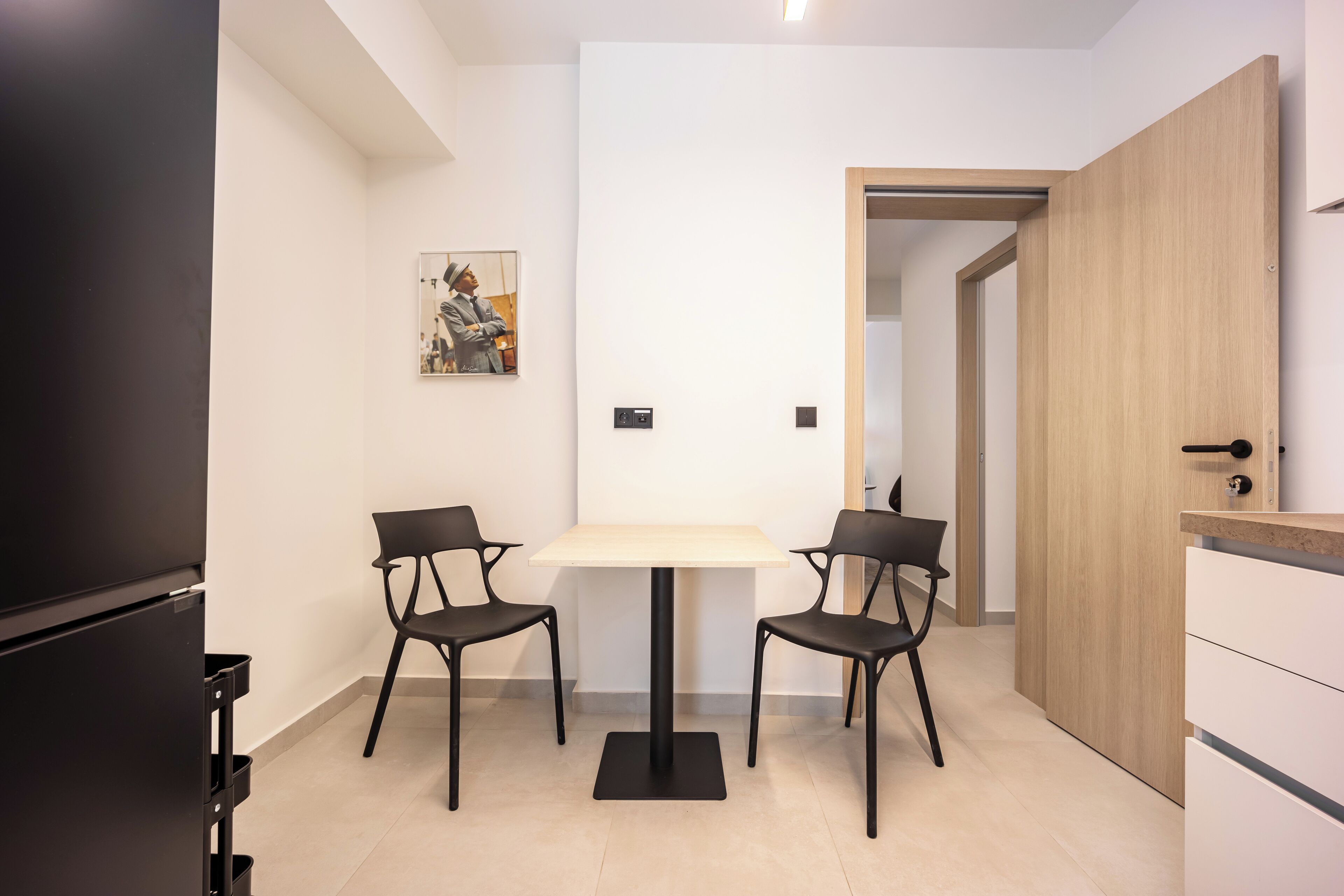 A modern kitchen with a dining table and chairs, a refrigerator, and a wooden door.