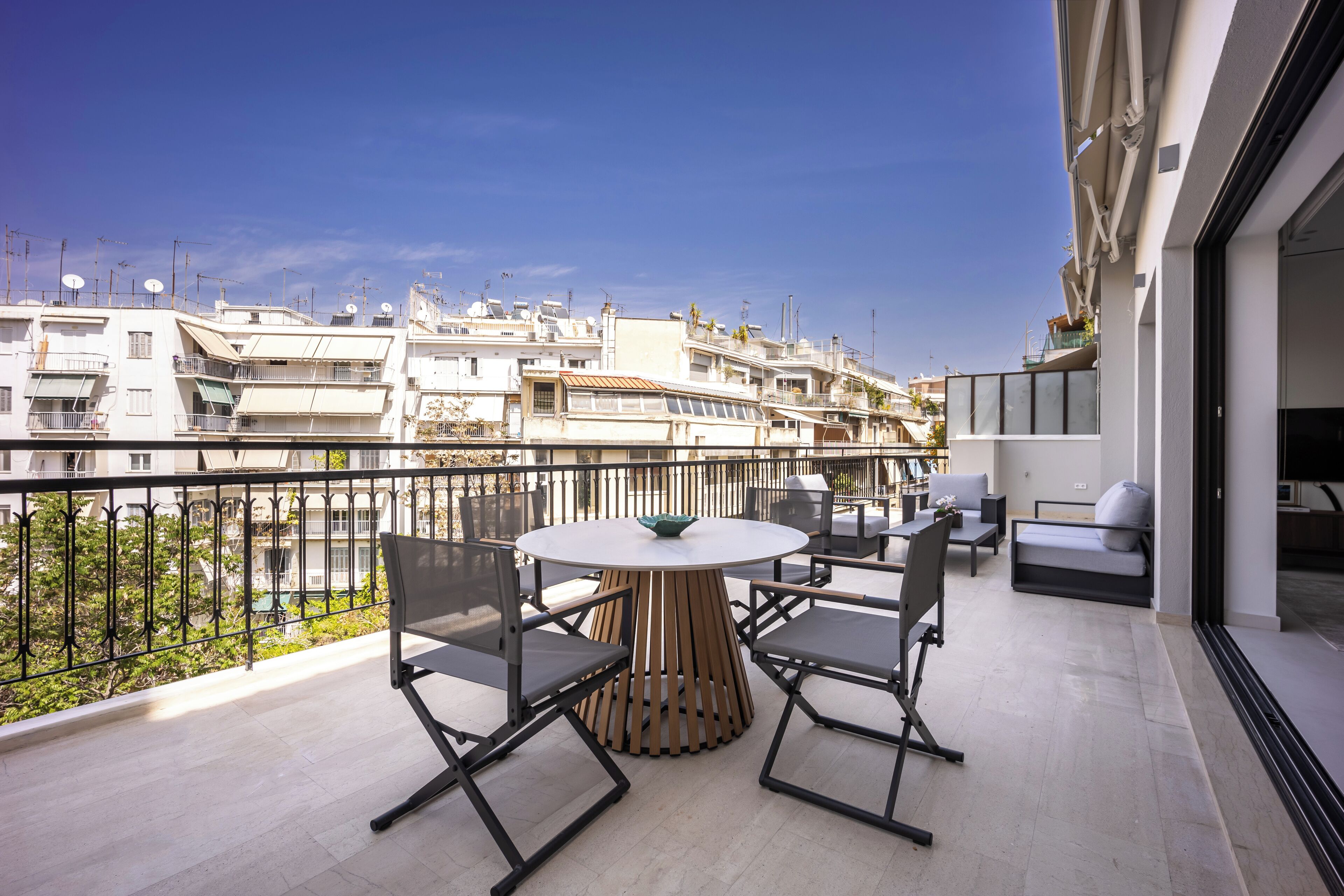 Een balkon met een ronde tafel en stoelen, met uitzicht op een woongebied met meerdere gebouwen.
