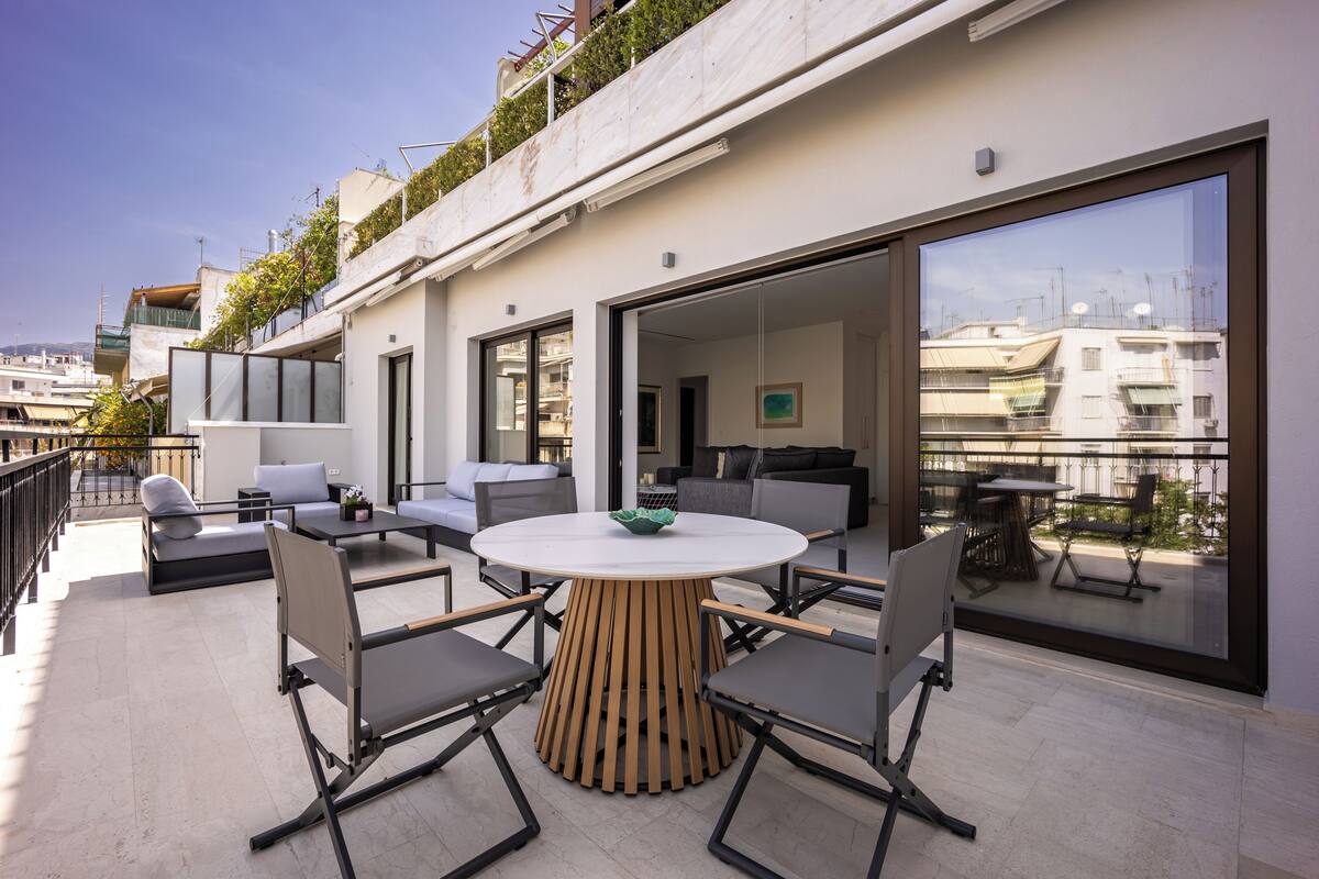 Um pátio moderno ao ar livre com mesa e cadeiras redondas, um sofá e uma varanda com vista para a cidade.