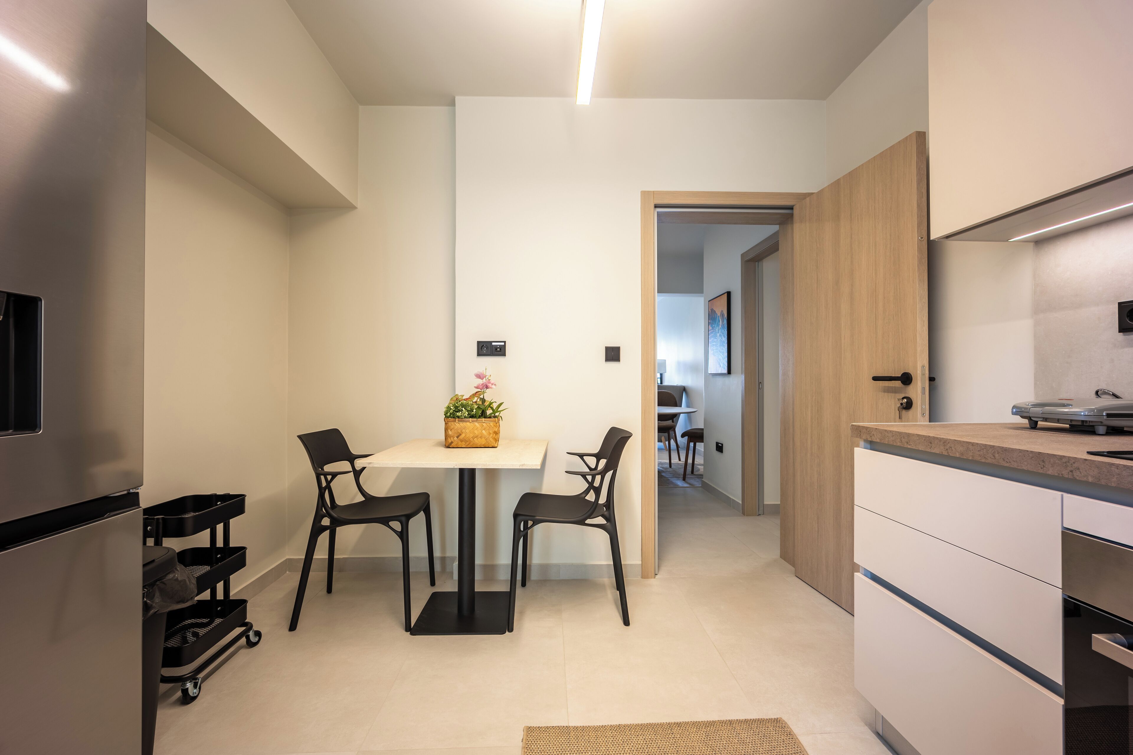 Cocina moderna con comedor, que incluye un refrigerador de acero inoxidable, un armario de madera y una pequeña mesa con sillas.