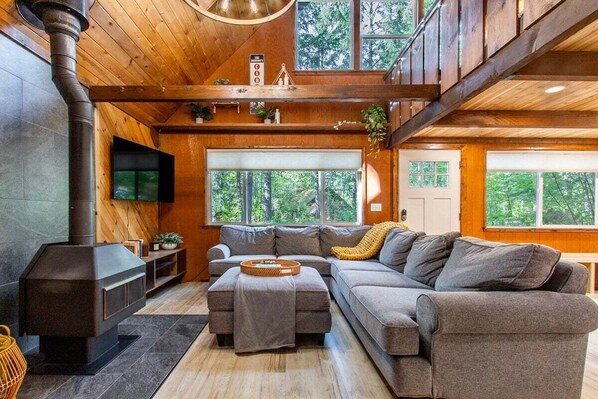Un salon chaleureux avec un grand canapé d’angle, une cheminée et un plafond en bois.