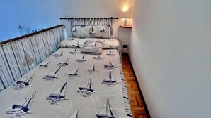 A narrow balcony with a bed featuring sailboat patterns, a railing, and a wall-mounted lamp. - Casa Ariel in the historic village. (Rio dell'Elba)