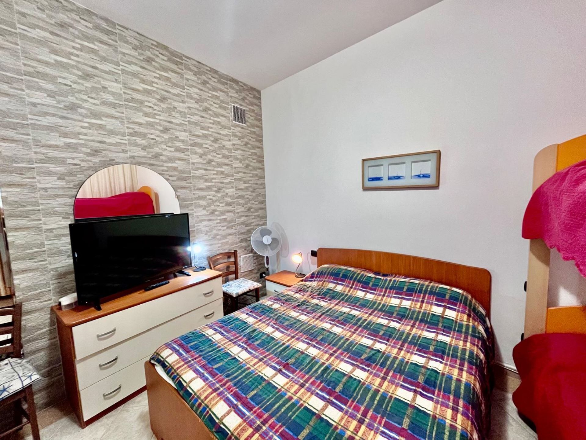 Una camera da letto con un letto, una televisione su un comò, una ventola e un quadro appeso al muro.