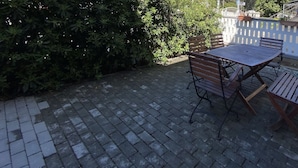 A patio with a table and chairs, surrounded by a brick floor and greenery.