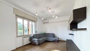 A spacious room with a grey sofa, wooden flooring, a large window, and a built-in shelf unit.