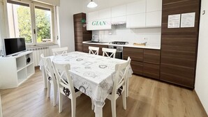 A modern kitchen with white cabinets, a dining table with a clock tablecloth, and a TV on a shelf.