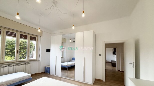 A modern bedroom with a large bed, a walk-in closet, and a view of a garden through the window.