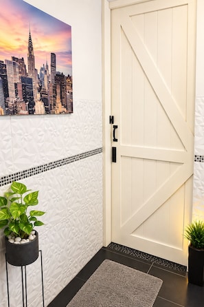 A white door with a diagonal handle, a cityscape painting above it, and two potted plants on either side.