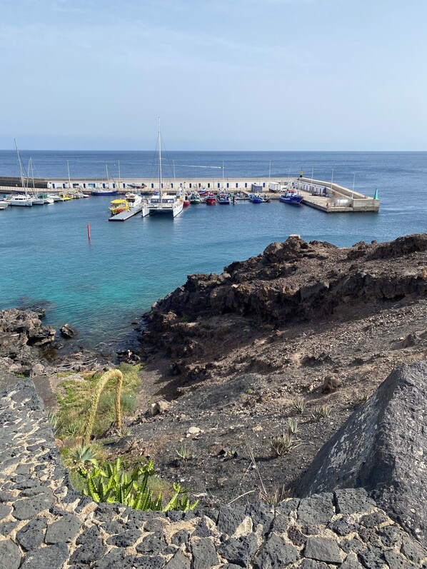 Un port de plaisance situé sur la côte, avec des bateaux amarrés, un terrain rocheux et un ciel dégagé.