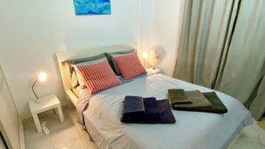 Une chambre à coucher bien rangée, avec un lit, des lampes de chevet, une petite table et une œuvre d’art accrochée au mur.