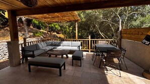 An outdoor patio with a wooden pergola, a sectional sofa, a dining table with chairs, and a stone wall. - La Villa Maquis, VILLA MAQUIS (Bonifacio)