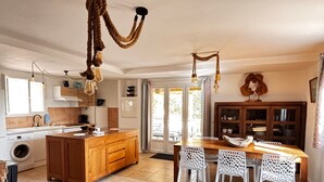 A spacious kitchen with a central island, wooden cabinets, and a dining area with white chairs. - La Villa Maquis, VILLA MAQUIS (Bonifacio)