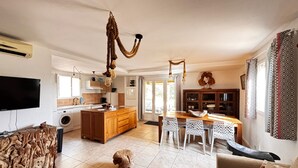 A spacious living area with a wooden coffee table, a sofa, and a dining table with chairs. There is a kitchen area with a washing machine and a dining table with a decorative bowl. - La Villa Maquis, VILLA MAQUIS (Bonifacio)