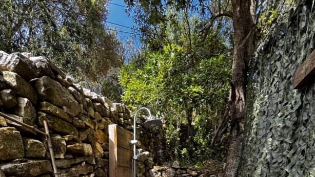 A rustic wooden cabin with a stone wall, a wooden ladder, and a metal barrel. - La Villa Maquis, VILLA MAQUIS (Bonifacio)