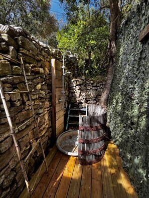 A rustic wooden cabin with a stone wall, a wooden ladder, and a metal barrel.