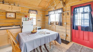 A wooden cabin interior with a dining table, chairs, a red door, and a refrigerator.