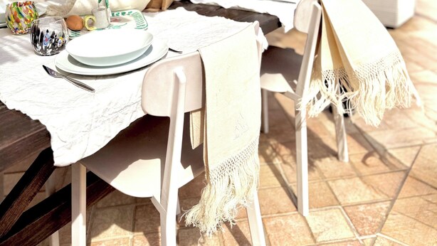 Mesa de comedor al aire libre con vista al mar y cactus, con mantel blanco, platos y una cesta de pan.