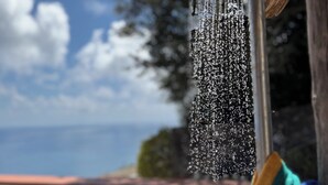 Un cabezal de ducha con agua corriendo, una estructura de madera y un cielo despejado con nubes.