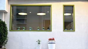 Een gevel met twee ramen, elk met een groene omlijsting. Er staan potplanten voor de ramen.