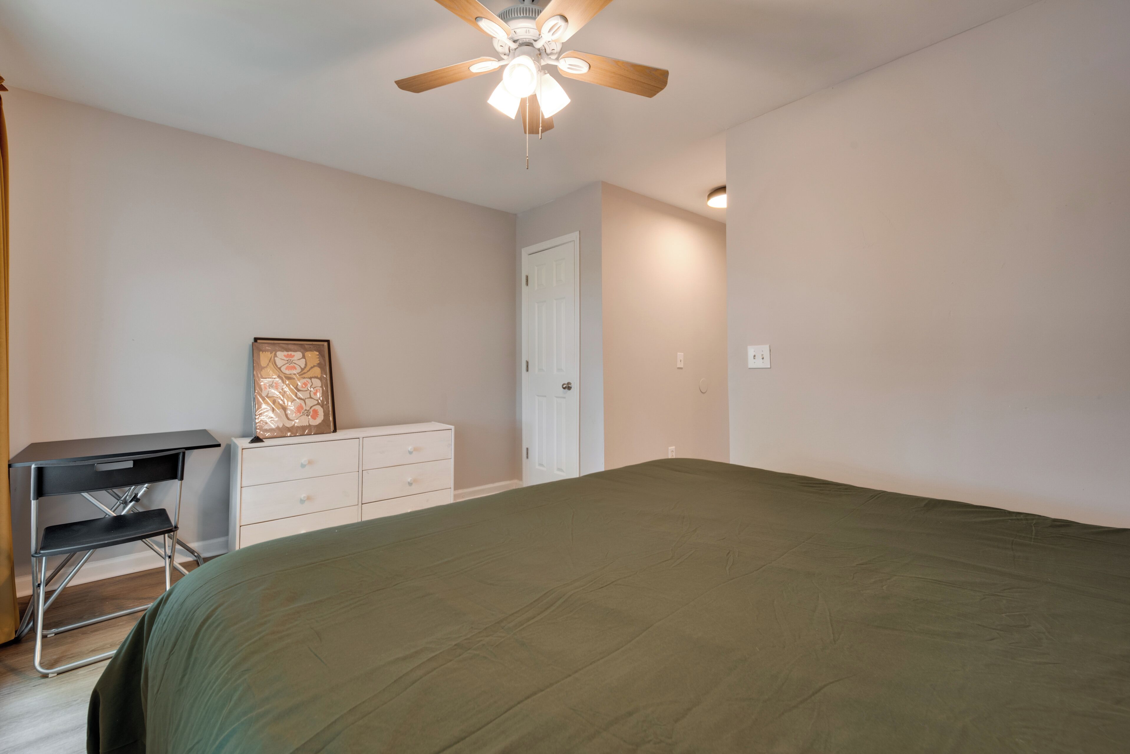 A bedroom with a bed, a desk, a chair, a dresser, and a ceiling fan.