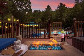 Eine Terrasse mit Feuerstelle, Sitzgelegenheit und einem Pool im Hintergrund.