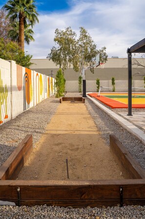 A sports court with a basketball hoop, surrounded by a gravel path and a wooden border.
