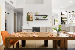 Una cocina moderna con armarios blancos, una mesa de comedor de madera con individuales y servilletas, y una planta en maceta sobre la encimera.