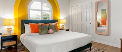 A bedroom with a bed, two bedside tables, a mirror, and a window with a yellow arch.