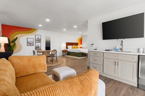 Een moderne hotelkamer met een bank, een bed, een televisie en een kitchenette.