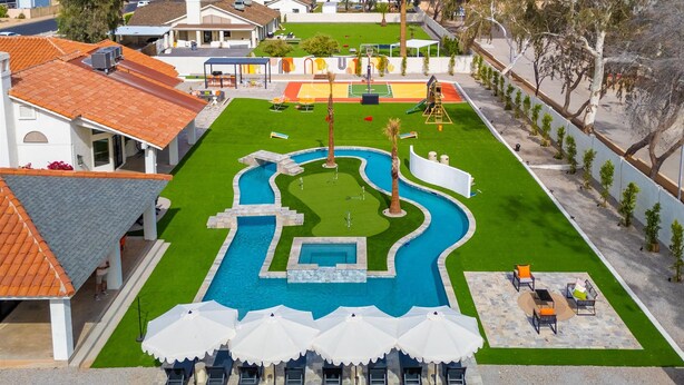Una piscina con una fuente, rodeada por un patio con sombrillas y sillones de descanso.