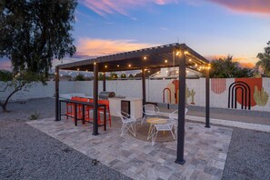 An outdoor patio with a grill, seating, and string lights.