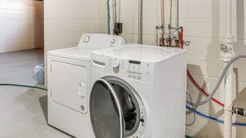 Une buanderie équipée de deux machines à laver et deux sèche-linge superposés, d’un tuyau d’arrosage et de la plomberie nécessaire.