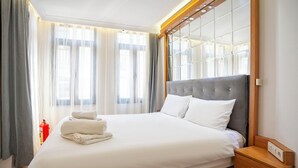 A neatly made bed with white linens and a grey headboard, a wooden nightstand with a drawer, and a fire extinguisher in the corner. - Viva Sirkeci Butik Otel (Istanbul)
