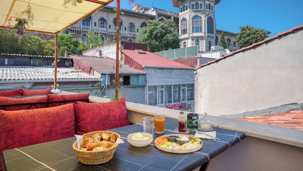 A rooftop restaurant with a view of a historic building, outdoor seating with red cushions, and a table set with food and drinks. - Viva Sirkeci Butik Otel (Istanbul)