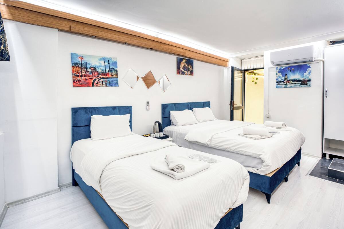 Una camera d'albergo con due letti, biancheria da letto bianca, soffitto in legno e opere d'arte alle pareti.