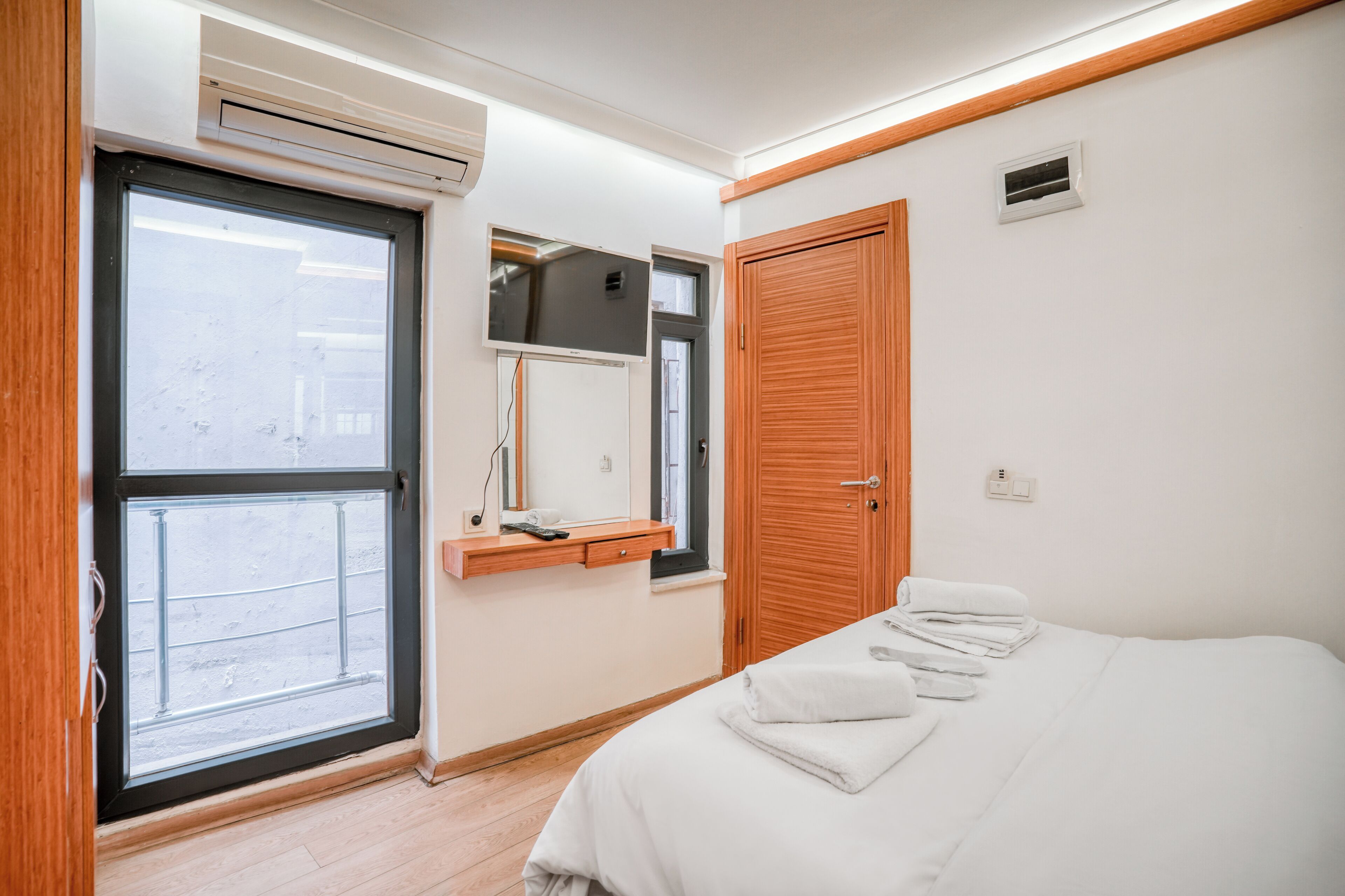A bedroom with a bed, a window, a mirror, and a wooden door.