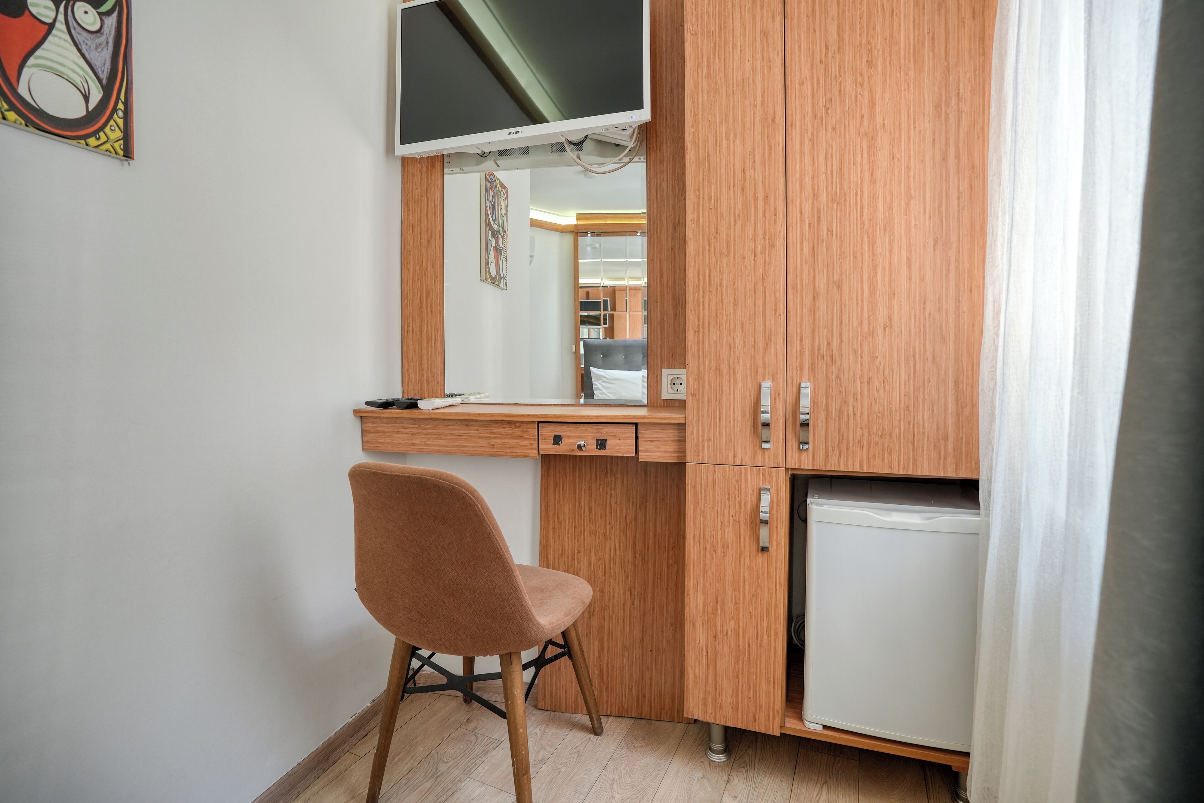 A small room with a wooden desk, a chair, a television, and a mini-fridge.
