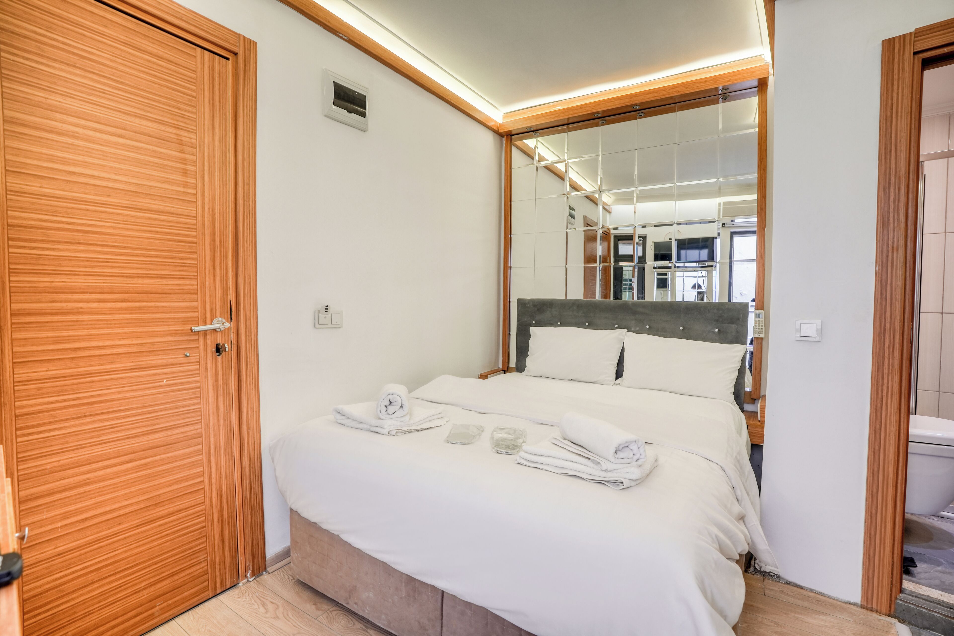Una habitación de hotel con un armario de madera, una cama con ropa blanca y un espejo grande que refleja el cuarto.